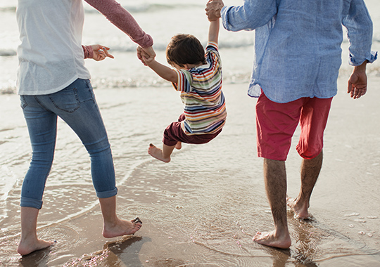 child swinging between parents hands, jumping waves on the beach